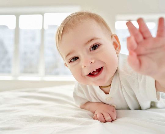 Ein Baby lacht in die Kamera und streckt dabei die Hand aus