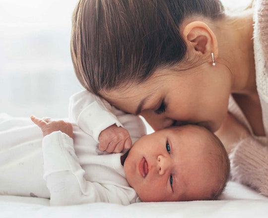 Ein Baby liegt auf einer Decke, während die Mutter ihm einen Kuss auf den Kopf gibt