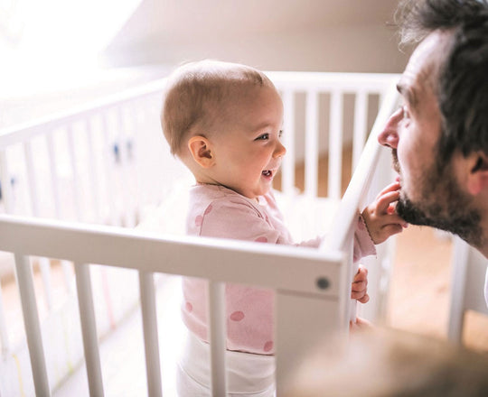 Baby steht im Gitterbett und greift nach seinem Papa