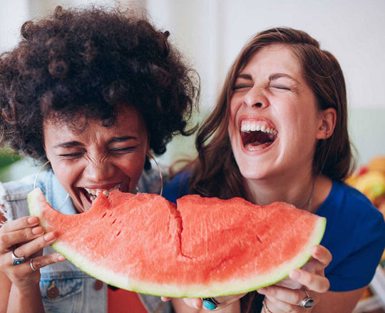 Zwei Frauen beißen lachend in eine Wassermelone