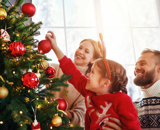 Mädchen schmückt gemeinsam mit ihren Eltern den Weihnachtsbaum