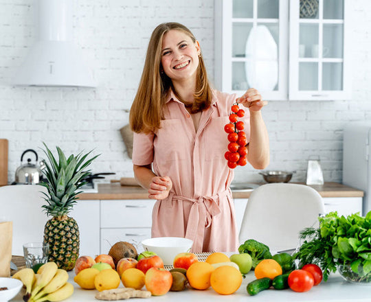 Frau steht in der Küche, vor ihr liegt eine Auswahl an buntem Obst und Gemüse