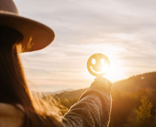 Frau hält ein lächelndes Gesicht gegen die Sonne
