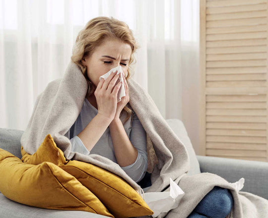 Eine Frau sitzt mit einer Decke auf dem Sofa und schnäuzt sich die Nase