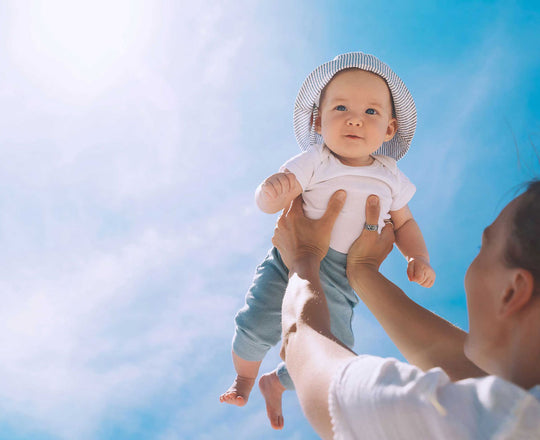ine Mutter hält ihr Baby mit ausgestreckten Armen hoch in die Luft