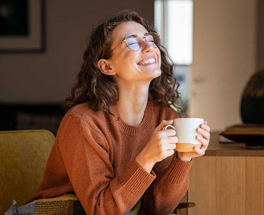 Frau sitzt mit einer Tasse auf dem Sofa und genießt die Sonne