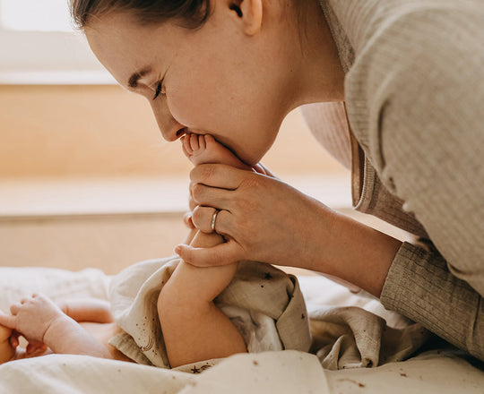 Eine Mutter hält die Füße ihres Babys, das vor ihr auf dem Rücken liegt.