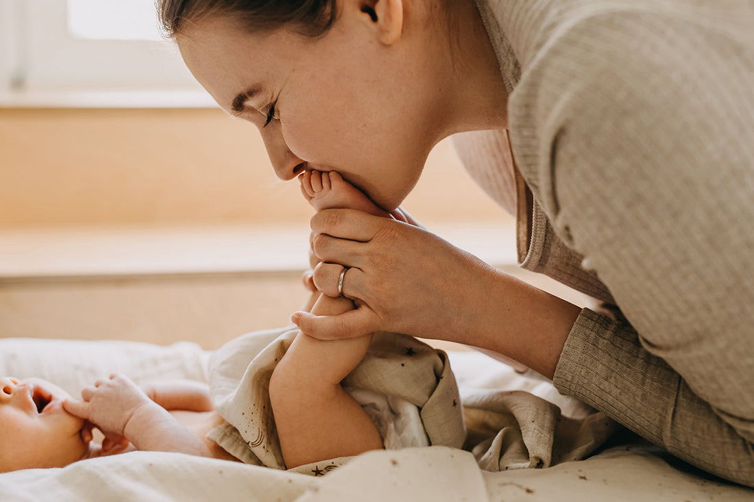 Eine Mutter hält die Füße ihres Babys, das vor ihr auf dem Rücken liegt.