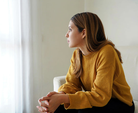 Frau sitzt auf einem Sofa und blickt deprimiert aus dem Fenster
