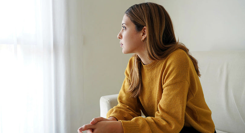 Frau sitzt auf einem Sofa und blickt deprimiert aus dem Fenster