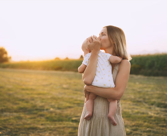 Eine Mama steht mit ihrem Baby im Arm auf einer Wiese