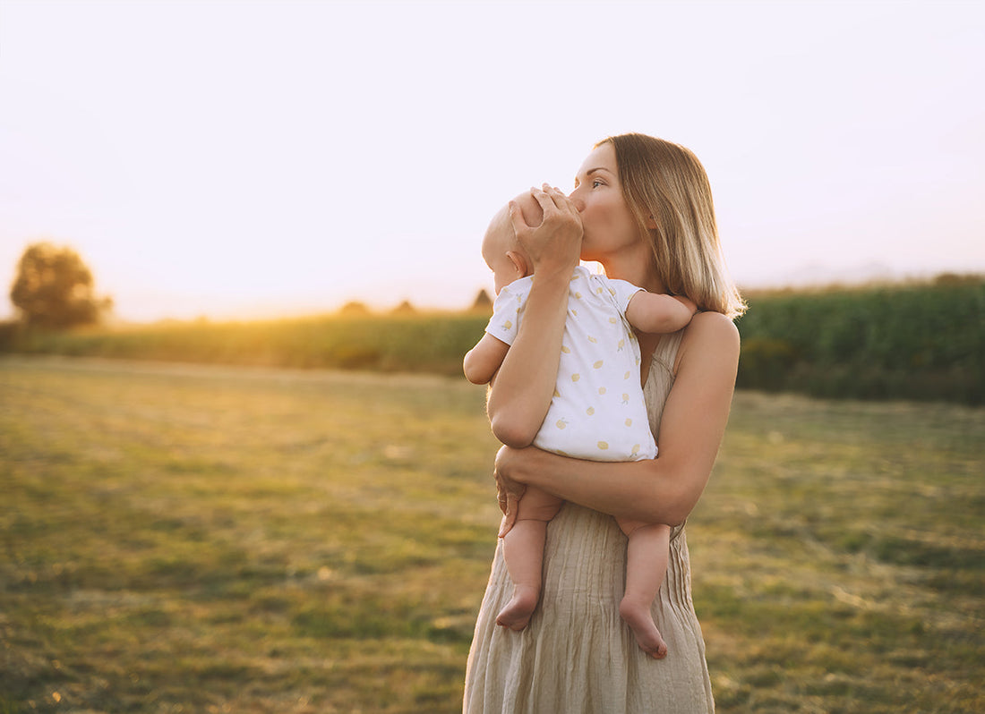 Eine Mama steht mit ihrem Baby im Arm auf einer Wiese