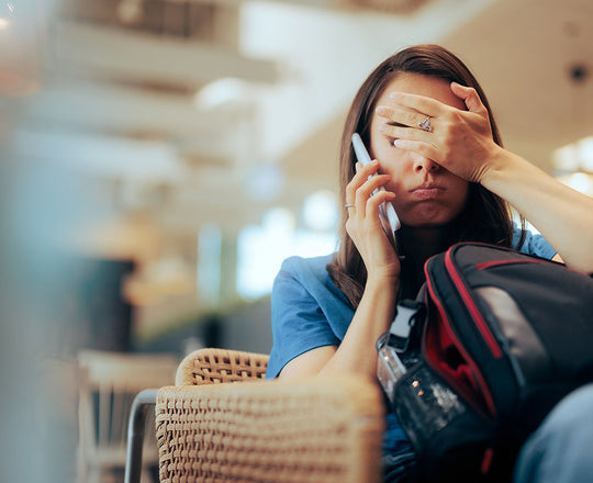 Eine erschöpfte Frau sitzt mit ihrem Gepäck am Flughafen