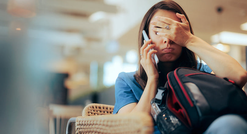 Eine erschöpfte Frau sitzt mit ihrem Gepäck am Flughafen