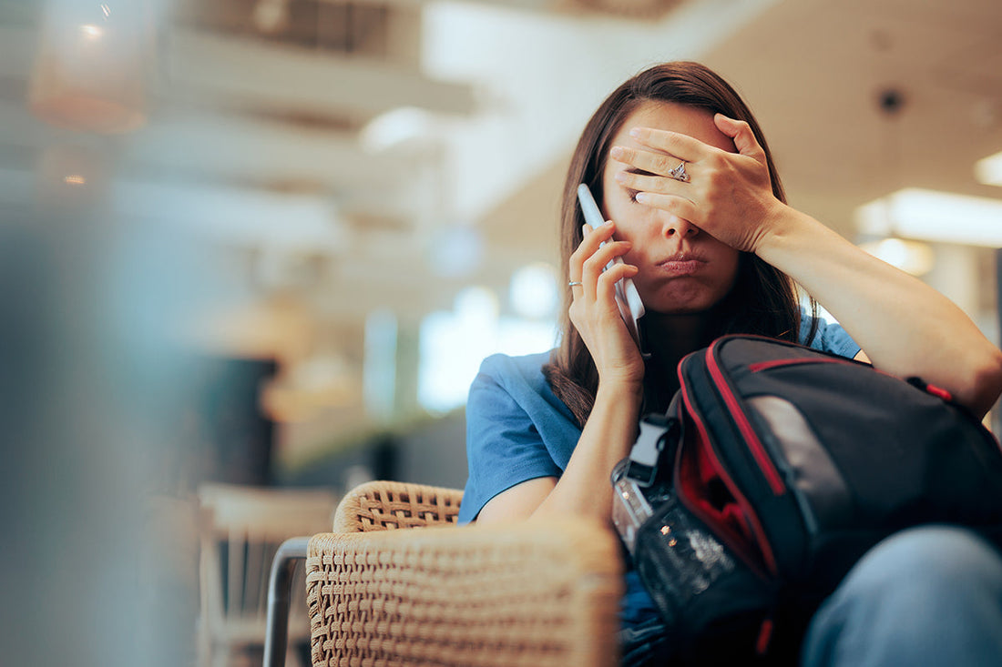 Eine erschöpfte Frau sitzt mit ihrem Gepäck am Flughafen