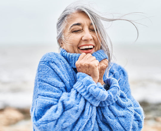 Frau steht mit geschlossenen Augen am Meer und atmet durch