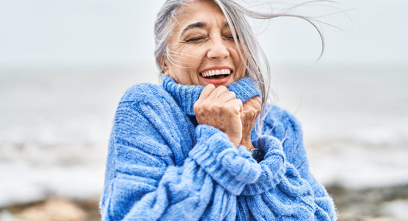 Frau steht mit geschlossenen Augen am Meer und atmet durch