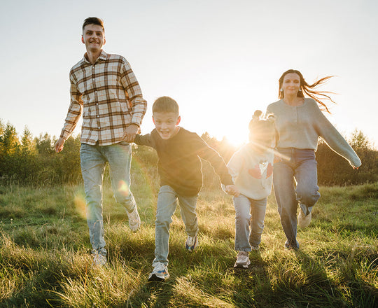Eine vierköpfige Familie läuft im Herbst über eine grüne Wiese