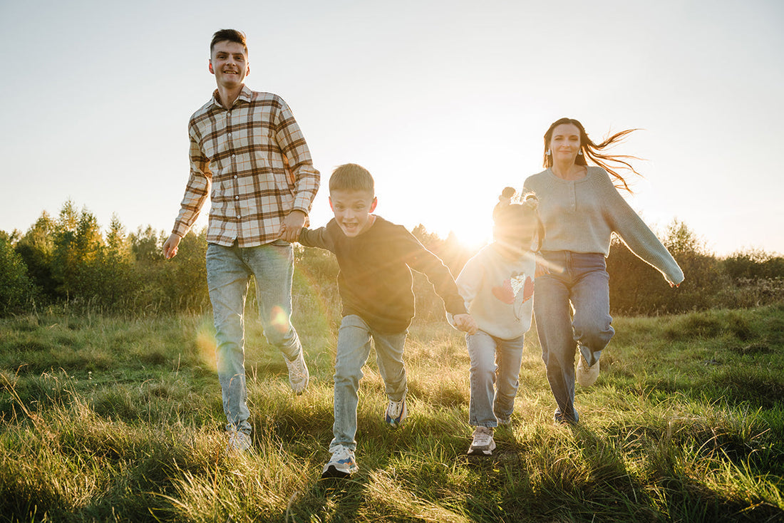Eine vierköpfige Familie läuft im Herbst über eine grüne Wiese