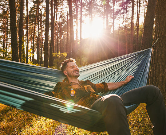 Mann sitzt in einer Hängematte in der Natur