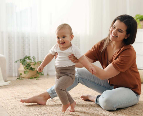 Mutter unterstützt ihre kleine Tochter, während sie zu Hause laufen lernt