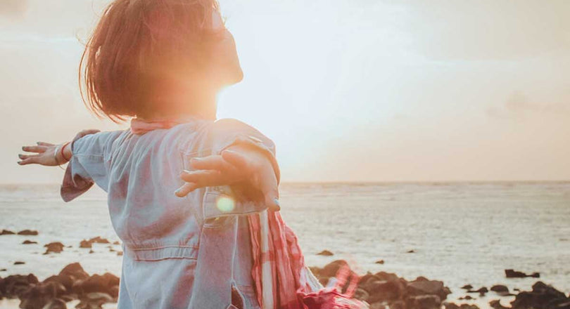 Frau steht am Meer und breitet die Arme aus