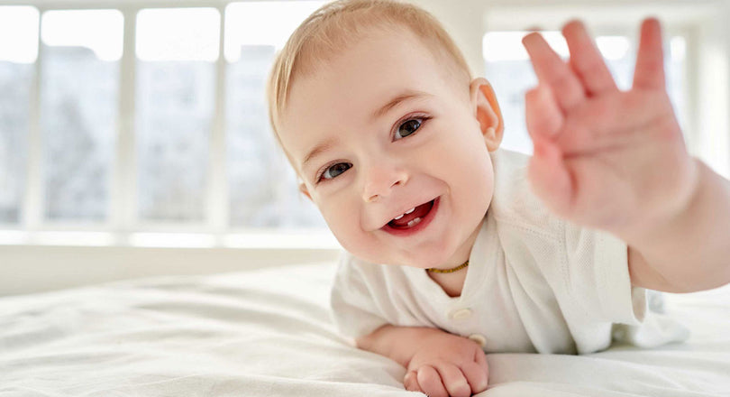 Ein Baby lacht in die Kamera und streckt dabei die Hand aus