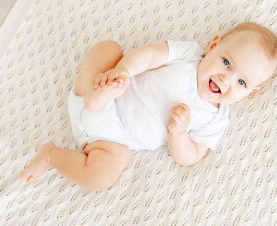 Ein Baby liegt auf einer Decke und greift mit der Hand nach seinem Fuß