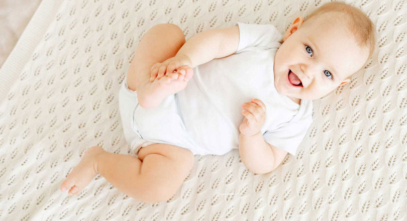 Ein Baby liegt auf einer Decke und greift mit der Hand nach seinem Fuß