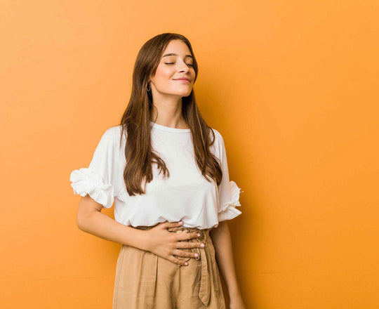 Eine Frau steht vor orangem Hintergrund und hält eine Hand auf ihrem Bauch