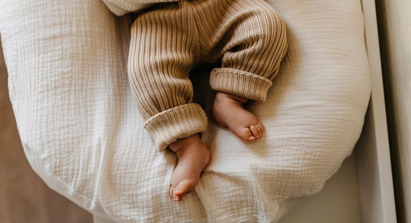 Ein Baby liegt auf einer beigen Unterlage, sichtbar sind nur die Beine und Füße