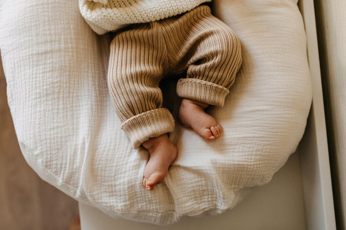 Ein Baby liegt auf einer beigen Unterlage, sichtbar sind nur die Beine und Füße