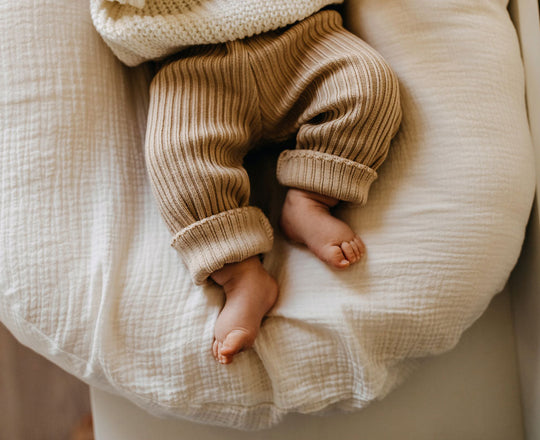 Ein Baby liegt auf einer beigen Unterlage, sichtbar sind nur die Beine und Füße