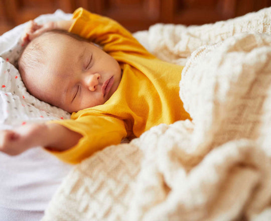 Baby liegt schlafend im Bett und hält die Hände über den Kopf gestreckt