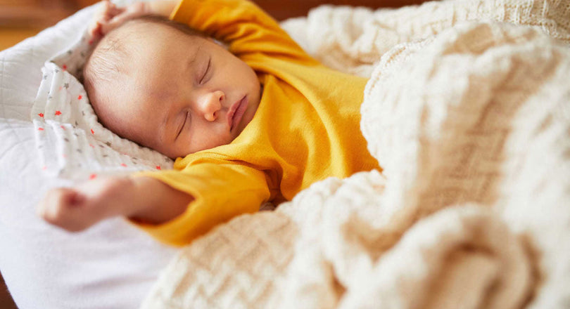 Baby liegt schlafend im Bett und hält die Hände über den Kopf gestreckt