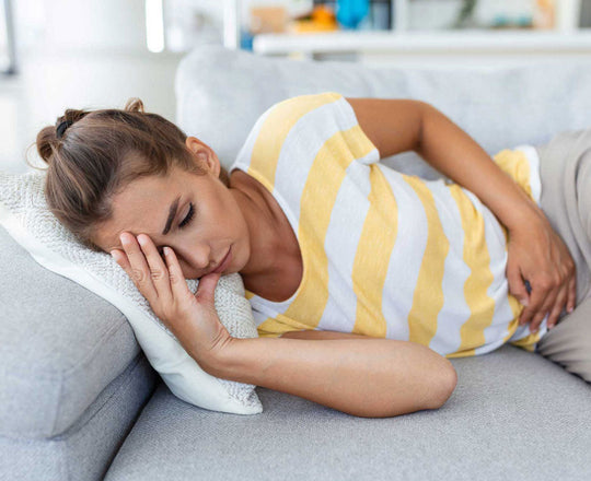 Frau liegt auf dem Sofa und hält sich den Bauch vor Schmerzen