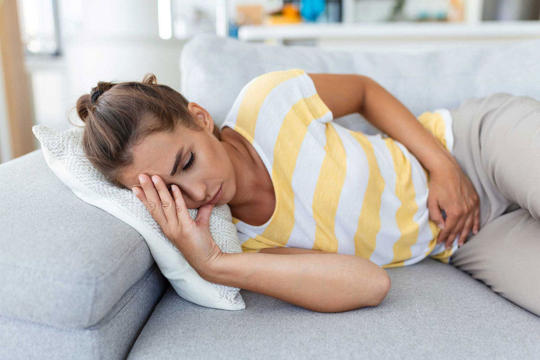 Frau liegt auf dem Sofa und hält sich den Bauch vor Schmerzen