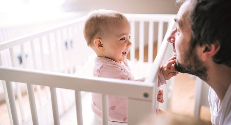 Baby steht im Gitterbett und greift nach seinem Papa
