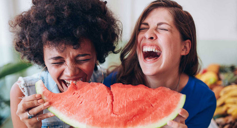 Zwei Frauen beißen lachend in eine Wassermelone