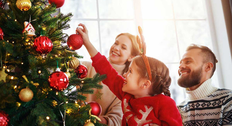 Mädchen schmückt gemeinsam mit ihren Eltern den Weihnachtsbaum
