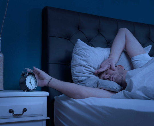 Ein Mann liegt im Bett und schaut verschlafen auf den Wecker