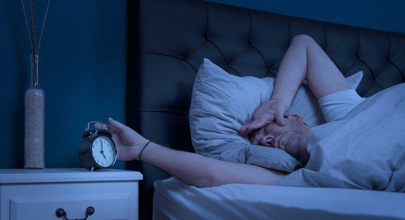 Ein Mann liegt im Bett und schaut verschlafen auf den Wecker