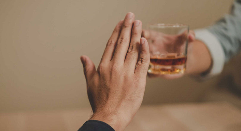 Eine Handgeste signalisiert Ablehnung gegenüber einem Glas mit alkoholischem Getränk