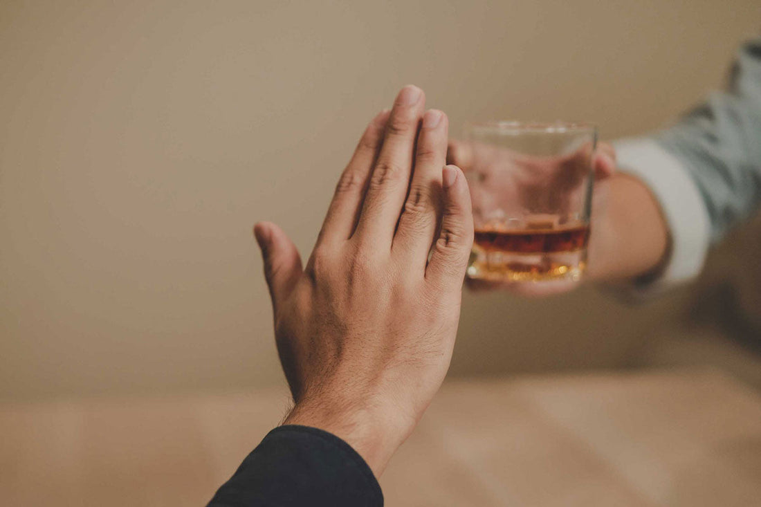 Eine Handgeste signalisiert Ablehnung gegenüber einem Glas mit alkoholischem Getränk