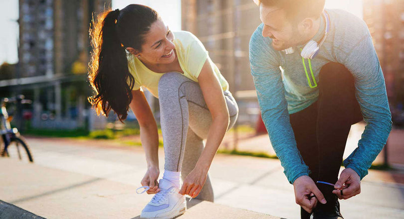 Frau und Mann binden sich die Schuhe, bevor sie joggen gehen