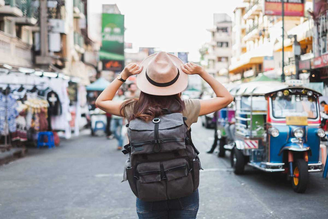Frau trägt Hut und Rucksack, während sie auf einer Straßen in Asien steht und die Umgebung betrachtet