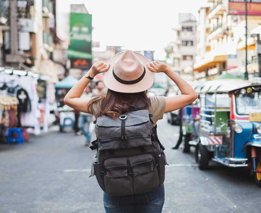 Frau trägt Hut und Rucksack, während sie auf einer Straßen in Asien steht und die Umgebung betrachtet