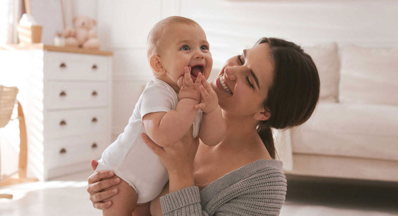 Eine Mama sitzt im Kinderzimmer auf dem Boden und hält ihr Baby in den Armen