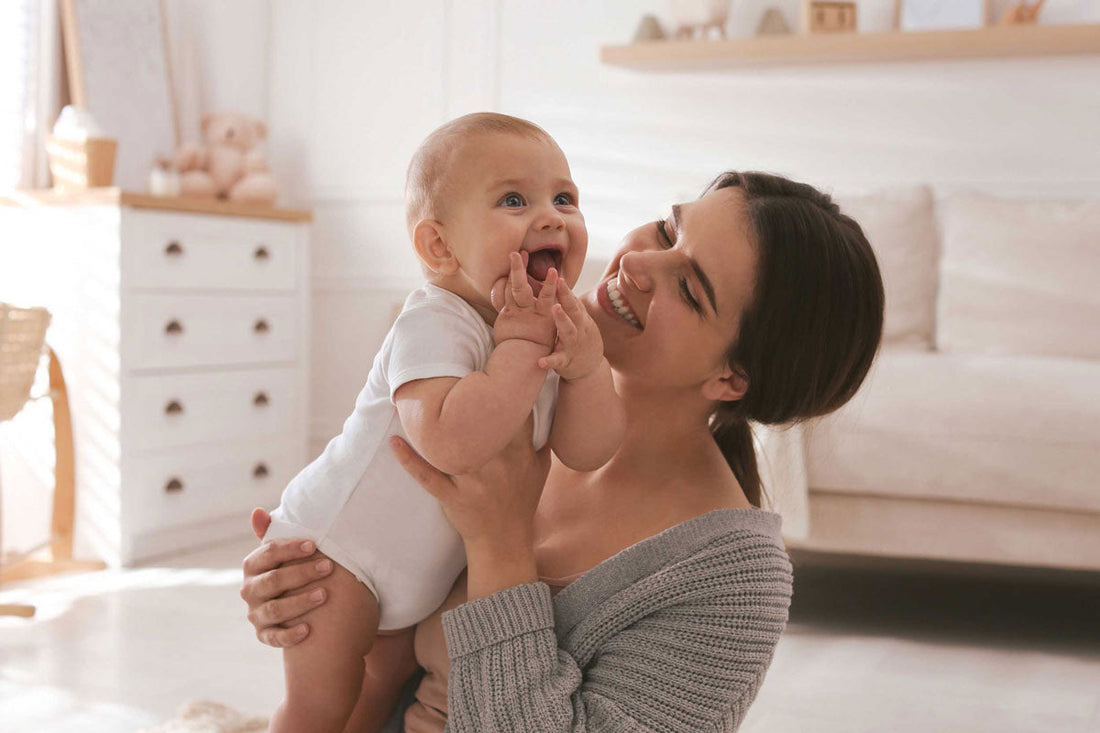 Eine Mama sitzt im Kinderzimmer auf dem Boden und hält ihr Baby in den Armen