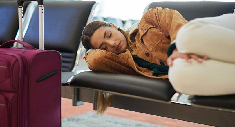 Eine Frau schläft auf einer Sitzbank am Flughafen, ihr Koffer steht vor ihr